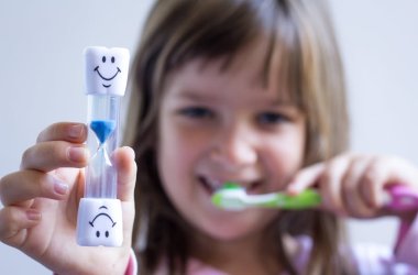 Child measures time while brushes her teeth. Healthy habits, dentalcare concept. Close up.