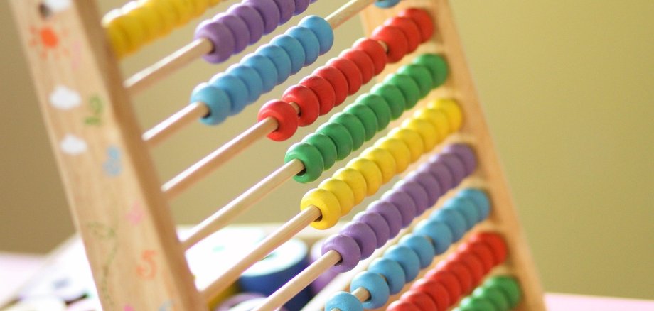 Symbolbild einer Zählmaschine/Abacus. Bunte Holzperlen sind auf einem Holzgestell aufgereiht.
