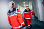 Rettungsdienst Rettungsdienstmitarbeiterinnen in einem langen Gang auf dem Weg zum Einsatz. Sie sind von hinten zu sehen und tragen auffällig rote Jacken.