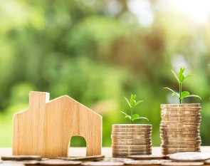 Geld Home Münzen Münzstapel, die neben einem Holzhaus aufgestapelt sind