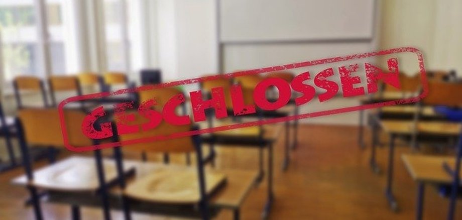 Symbolbild geschlossene Schule. Ein leerer Klassenraum ist zu sehen. Die Stühle stehen auf den Tischen. Über das Bild ist der Schriftzug "Geschlossen" montiert.