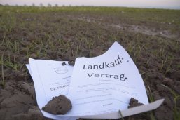 Auf Acker liegt symbolisch ein Kaufvertrag
