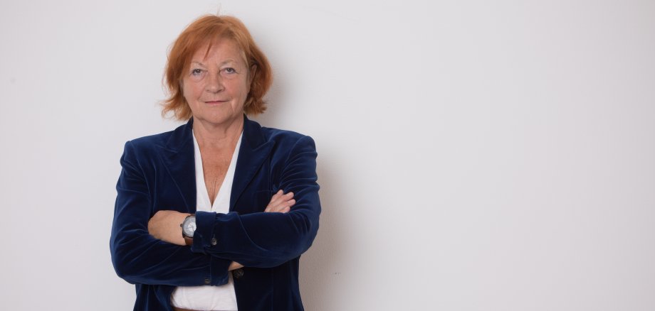 Elisabeth Hillebrand schaut mit verschränkten Armen in die Kamera. Sie trägt einen dunkelblauen Blazer.