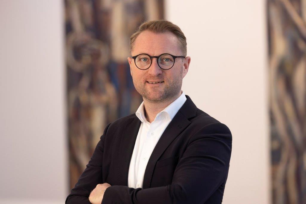 Porträtfoto  von Landrat Dr. Jens Mischak. Er schaut mit verschränkten Armen in die Kamera.