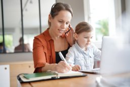 Mother working from home on computer with her young daughter Mother working from home on computer with her young daughter