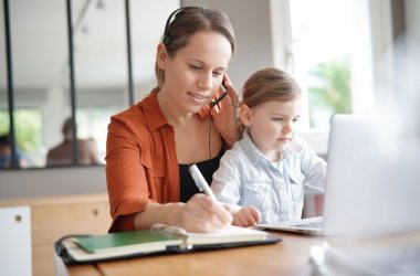 Mother working from home on computer with her young daughter