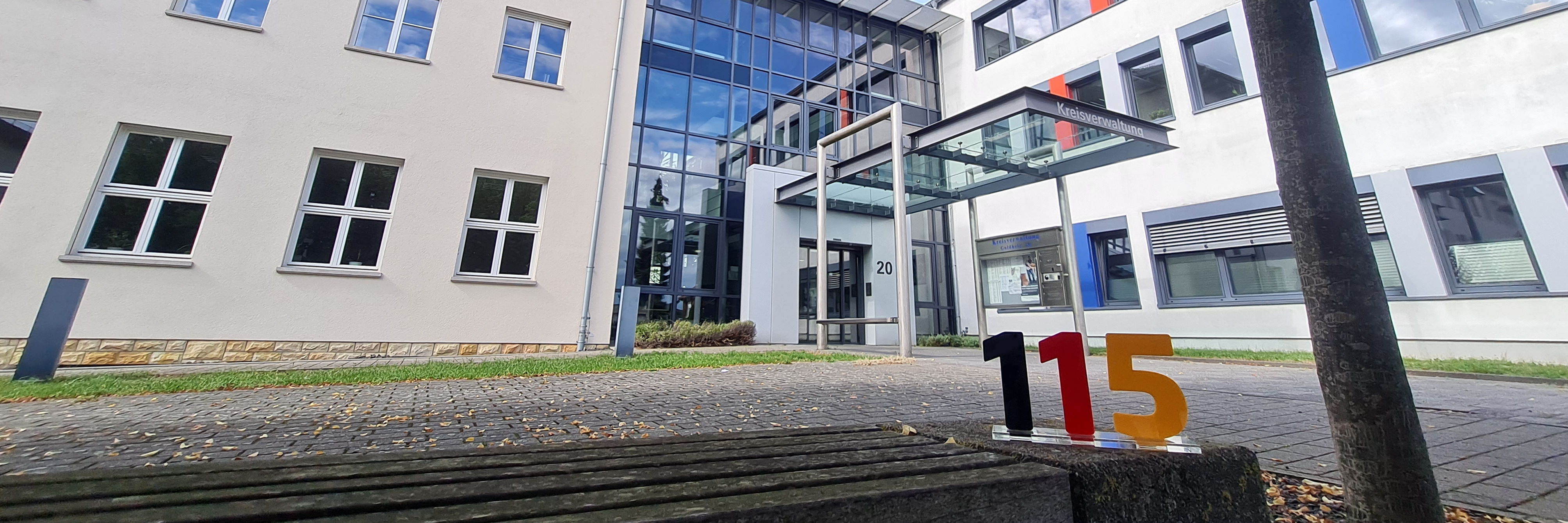 Eingangsbereich der Kreisverwaltung. im Vordergrund ist eine Sitzbank zu sehen. 