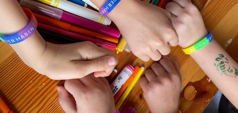 Kinderhände mit bunten Armbändern über einem Tisch mit Buntstiften
