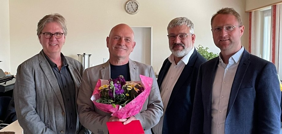 Erster Kreisbeigeordneter Dr. Jens Mischak, Tobias Hoffmann (Geschäftsführung Haus Kirschberg) und Helmut Benner, stellvertretender Leiter des Jugendamtes (von rechts), verabschieden Harry Bernardis und würdigen dessen Verdienste in der Jugendhilfe. Sie haben sich für ein Gruppenbild aufgestellt, Herr Bernardis hält einen Blumenstrauß und eine Grußkarte in den Händen