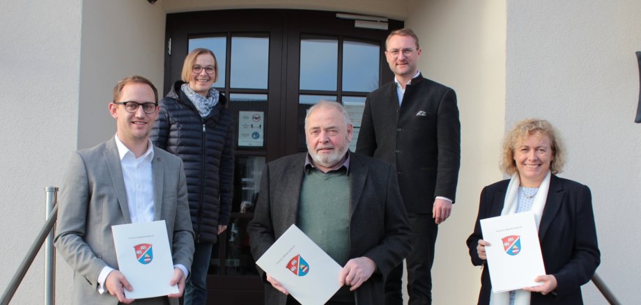 Fünf Menschen stehen auf einer Treppe vor der Verwaltung. in der vorderen Reihe stehen  Bürgermeister Leopold Bach, Stadtrat Willy Kreuzer und Bürgermeisterin Claudia Blum. Sie haben die Bewilligungsbescheide aus den Händen des Ersten Kreisbeigeordneter Dr. Jens Mischak und Angelika Boese, der Sachgebietsleiterin Dorfentwicklung, in Empfang genommen.