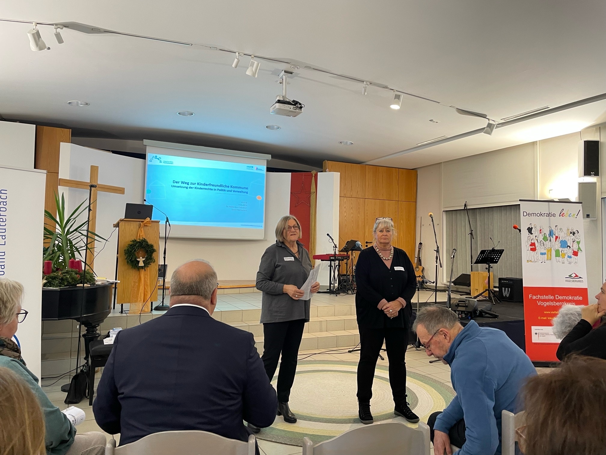 Zwei Frauen stehen vor einem Plenum und halten eine kurze Ansprache. 