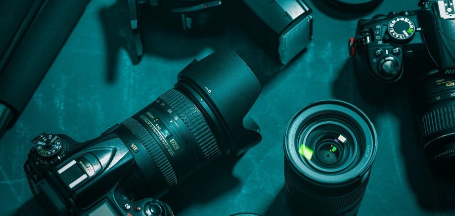Fotozubehör ist auf einem Tisch ausgebreitet. Darunter ein Fotoapparat und verschiedene Objektive.