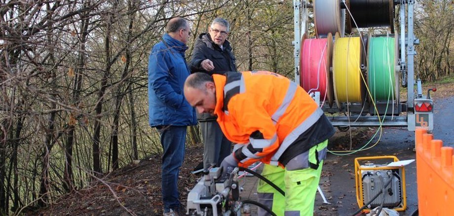 Ein Bauarbeiter bedient eine MAschine zum verlegen von Glasfaserkabeln. Gleich sieben Kabel werden am Stadtrand von Ulrichstein mit Druckluft in ein Leerrohr geblasen. Durch eine der bunten Röhren wird dann das Glasfaserkabel nach Feldkrücken führen, denn „Schritt für Schritt werden auch die kleinen Dörfer im Vogelsbergkreis mit schnellem Internet versorgt“, betont Landrat Manfred Görig beim Besuch auf der Baustelle.