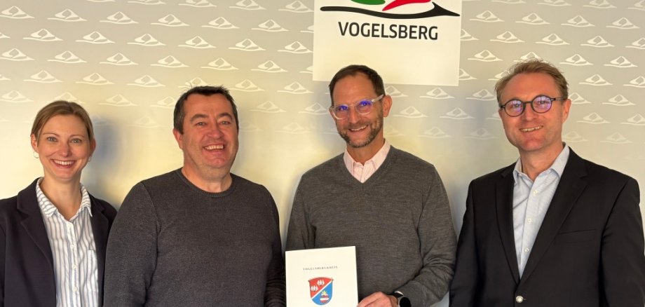 Landrat Dr. Jens Mischak und Jana Brittner, die Sachgebietsleiterin für Dorf- und Regionalentwicklung, übergeben Lauterbachs Bürgermeister Holger Marx (Zweiter von rechts) und Bernd Ruhl, in der Verwaltung zuständig für den Bereich Dorfentwicklung (Zweiter von links), den Bewilligungsbescheid.