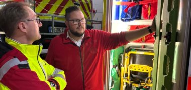 Notfallsanitäter Benedikt Geiger (rechts) erläutert Landrat Dr. Mischak die verschiedenen Ausrüstungsgegenstände im RTW – hier etwa eine Rettungstrage, wie sie beispielsweise bei Unfällen zum Einsatz kommen kann.