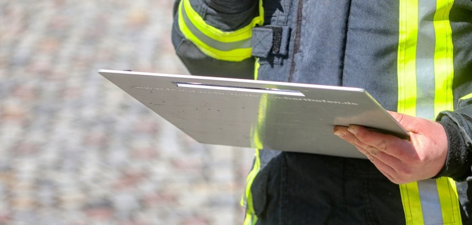 Ein Mensch mit Feuerwehrschutzkleidung hält ein Klemmbrett in der Hand. 