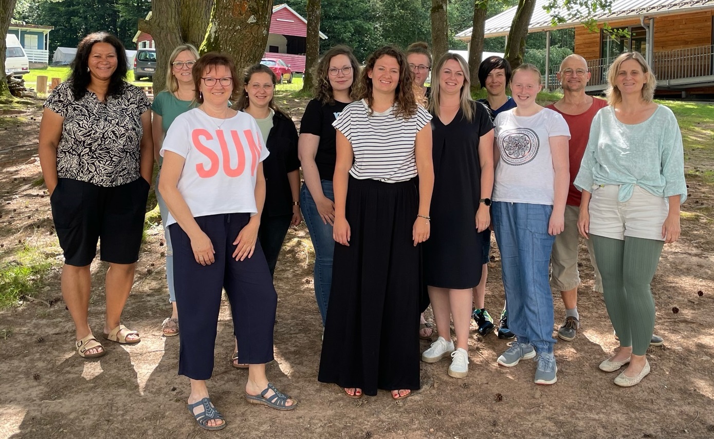 Zwölf Menschen haben sich im Kreisjugendheim in Landenhausen zum Gruppenbild aufgestellt. Sie stehen vor einer Baumgruppe.