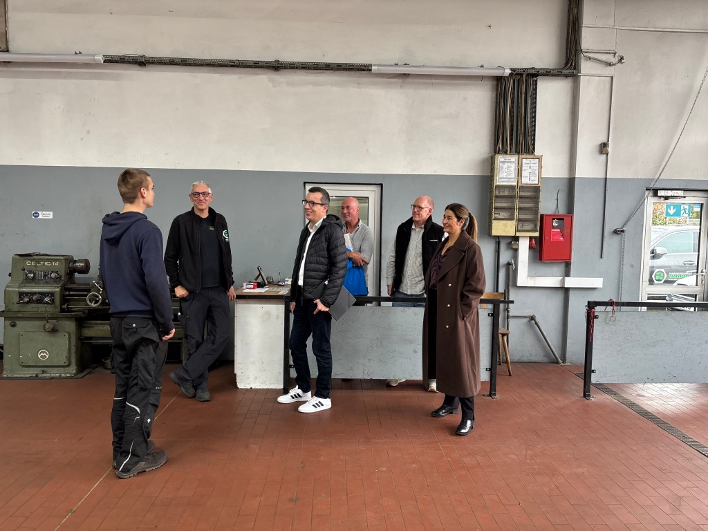 Jan (links) berichtet von seinem Arbeitsalltag beim Fahrzeugservice Riegelmann – Alsfelder Bremsendienst. Patrick Krug (dritter von links), Erster Kreisbeigeordneter sowie Schul- und Sozialdezernent, sowie Katja Diehl (von rechts), Vorstandsvorsitzende von Kompass Leben e.V., Lars Kersten, Lehrer an der Brüder-Grimm-Schule in Alsfeld, Michael Dippel, Werkstattleiter von Kompass Leben e.V., und Stefan Riegelmann, Inhaber vom Fahrzeugservice Riegelmann Alsfelder Bremsendienst, hören gespannt zu.