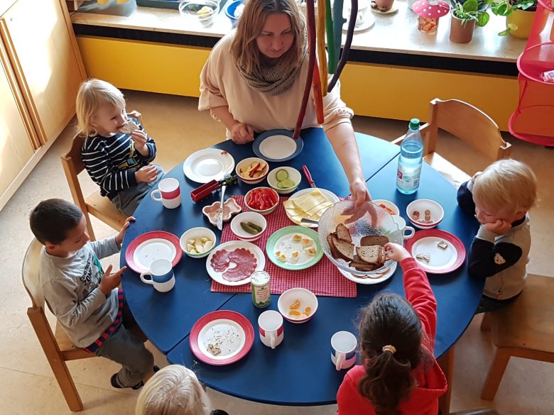Kinder sitzen gemeinsam an einem runden Tisch und frühstücken gemeinsam. 