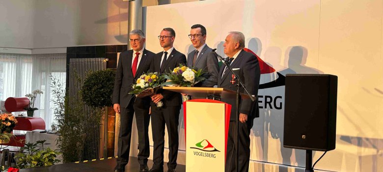 Manfred Görig, Dr. Jens Mischak, Patrick Krug und Dr. Hans Heuser stehen auf einer Bühne vor einer weißen Wand. Sie tragen Anzüge und lächeln in die Kamera