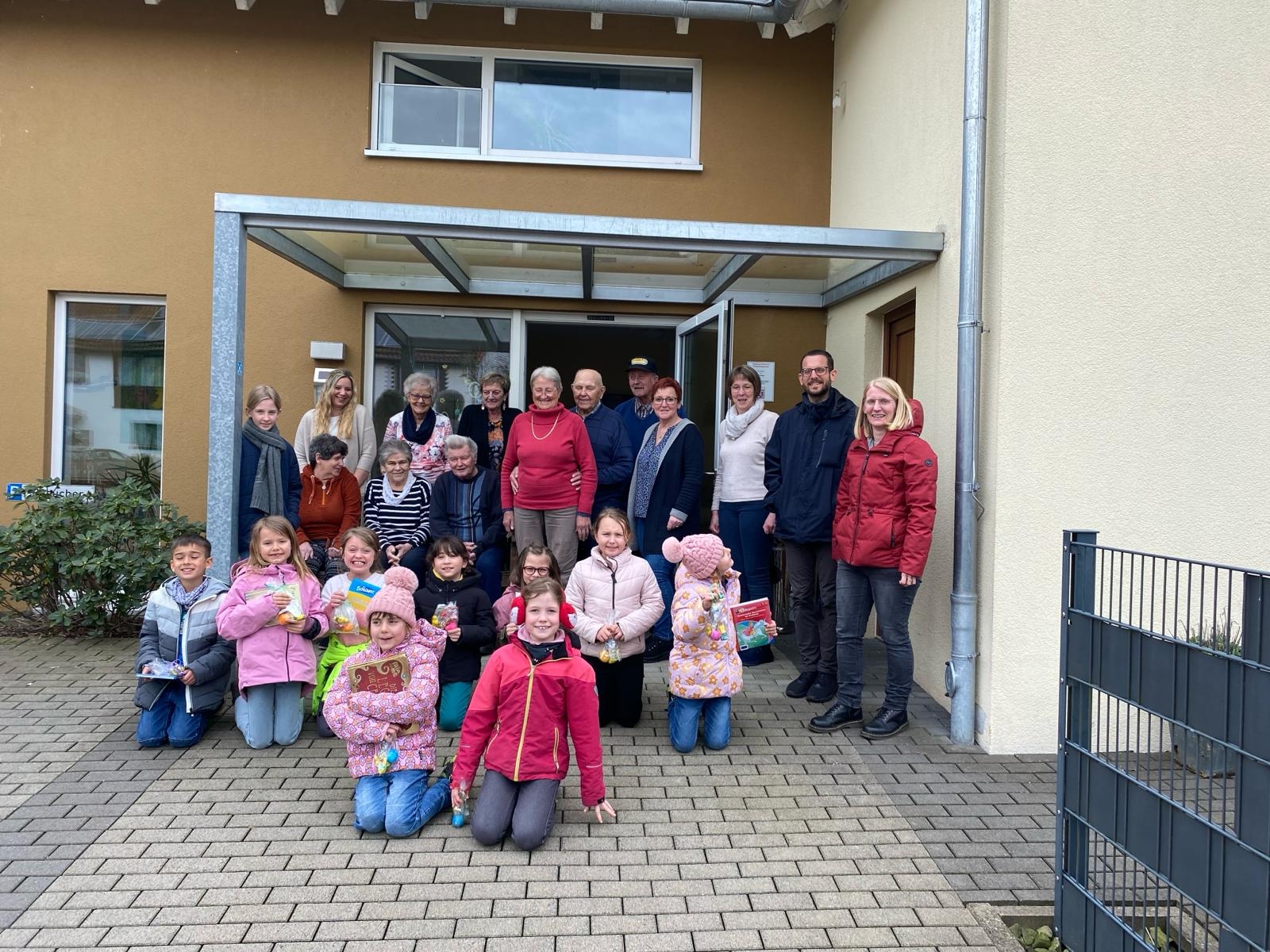 Abschlussbild vor dem Eingang: Senioren und Kinder haben sich gemeinsam für ein Gruppenbild aufgestellt und schauen in die Kamera.