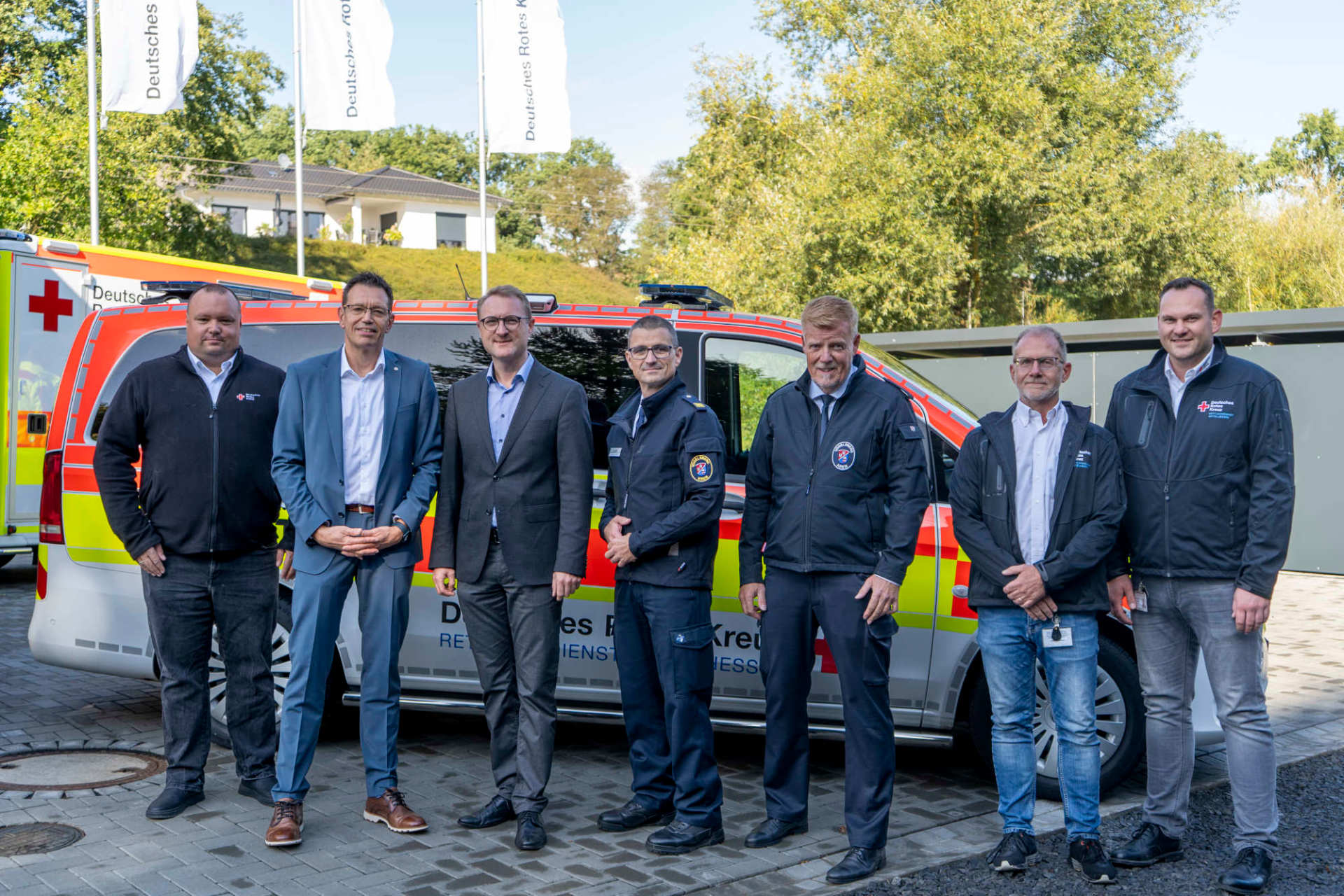 Mehrere Männer stehen vor einem Notarzteinsatzfahrzeug und schauen froh in die Kamera.