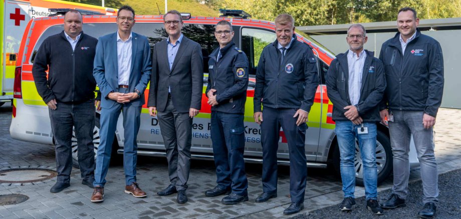 Mehrere Männer stehen vor einem Notarzteinsatzfahrzeug und schauen froh in die Kamera.