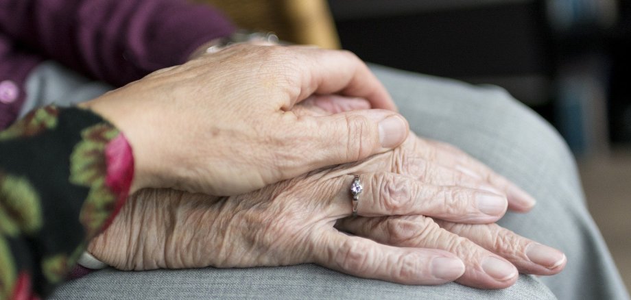 Pflege von älteren Menschen, jüngere Hand liegt auf älterer Hand