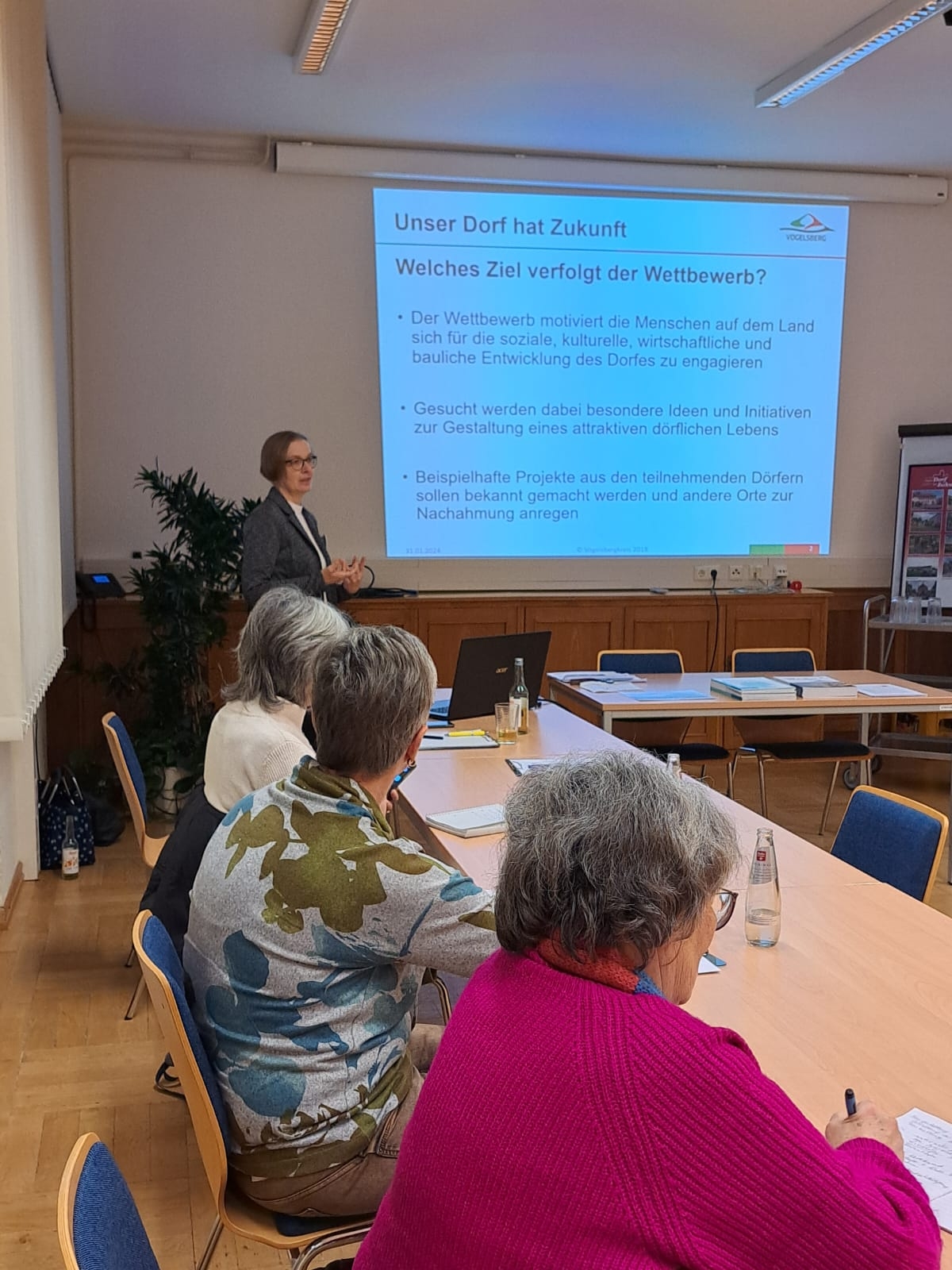 Angelika Boese hält einen Vortrag. Sie steht vor einer Leinwand und spricht.