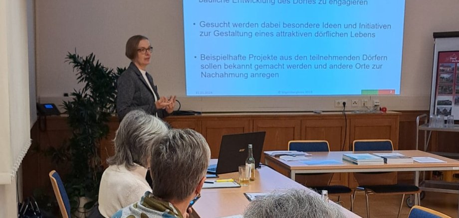 Angelika Boese hält einen Vortrag. Sie steht vor einer Leinwand und spricht.