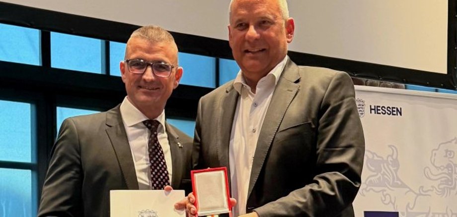 Kreisbrandinspektor Marcell Büttner und Innenminister Roman Poseck lächeln in die Kamera.