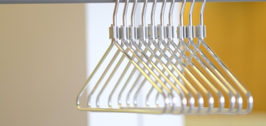 Mehrere Metallkleiderbügel hängen auf einer Kleiderstange. Kleidungsstücke sind nicht zu sehen. 