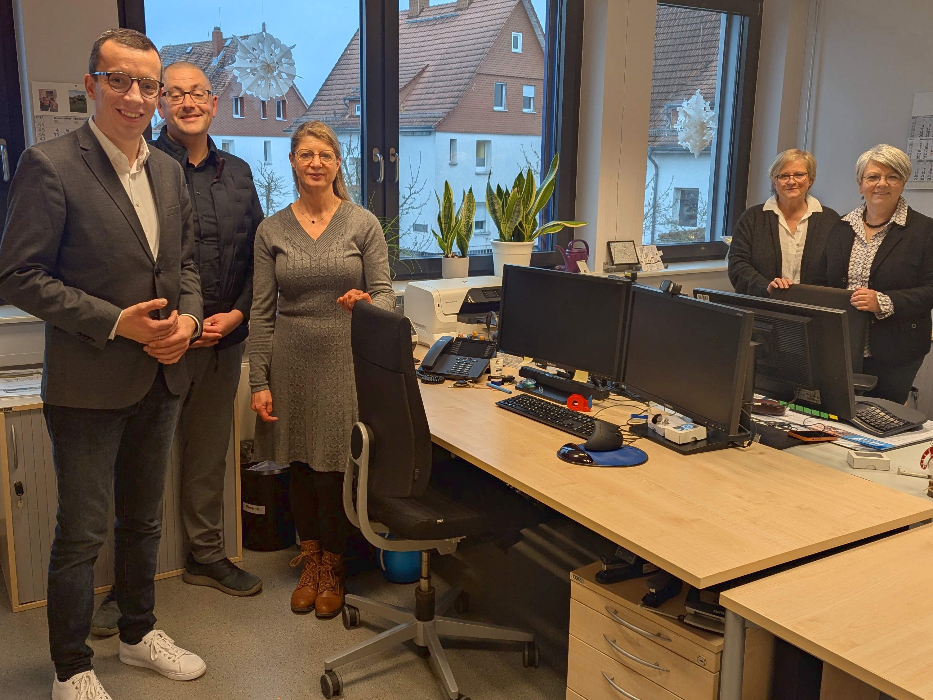 Fünf Menschen stehen zum Gruppenfoto rund um zwei Schreibtische in einem Büro. Erster Kreisbeigeordneter und Sozialdezernent Patrick Krug (links), beim Besuch in der Schuldnerberatungsstelle. Elke Diehl (von rechts), Yvonne Steller und Ina Sachs von der Schuldnerberatung sowie der Leiter des Sachgebiets Soziale Dienste im Amt für Soziales und Ausländerrecht, Bastian Heck, berichten aus dem Alltag. 