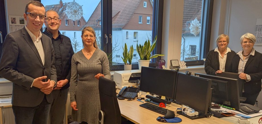 Fünf Menschen stehen zum Gruppenfoto rund um zwei Schreibtische in einem Büro. Erster Kreisbeigeordneter und Sozialdezernent Patrick Krug (links), beim Besuch in der Schuldnerberatungsstelle. Elke Diehl (von rechts), Yvonne Steller und Ina Sachs von der Schuldnerberatung sowie der Leiter des Sachgebiets Soziale Dienste im Amt für Soziales und Ausländerrecht, Bastian Heck, berichten aus dem Alltag. 