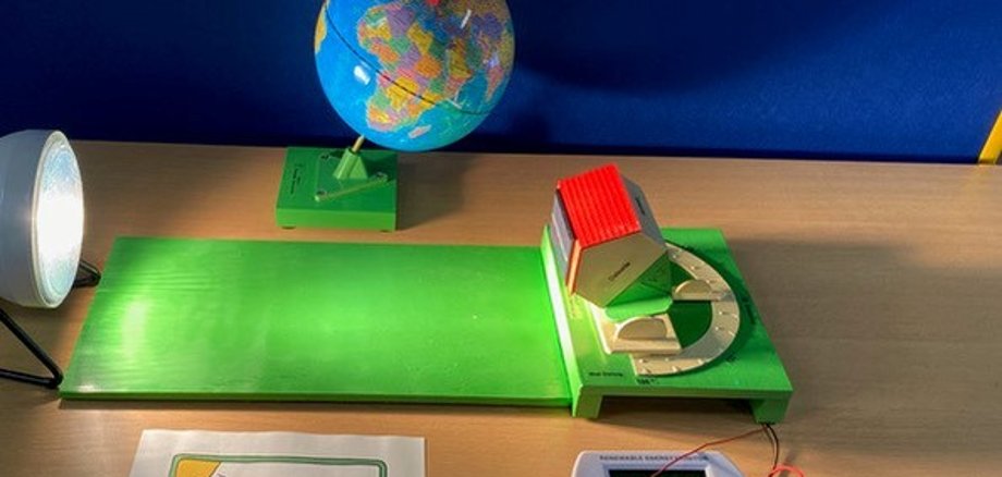 Eine Lampe, ein kleiner Globus und ein Modell eines Hauses mit Photovoltaikanlage zum Erläutern der Stromerzeugung auf einem Hausdach