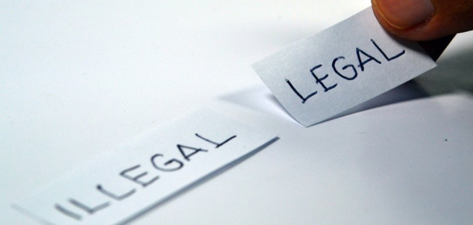 Zwei Finger legen einen Papierstreifen mit dem Wort "legal" auf einen Tisch. Dort liegt bereits ein Streifen mit dem Word "legal" darauf.