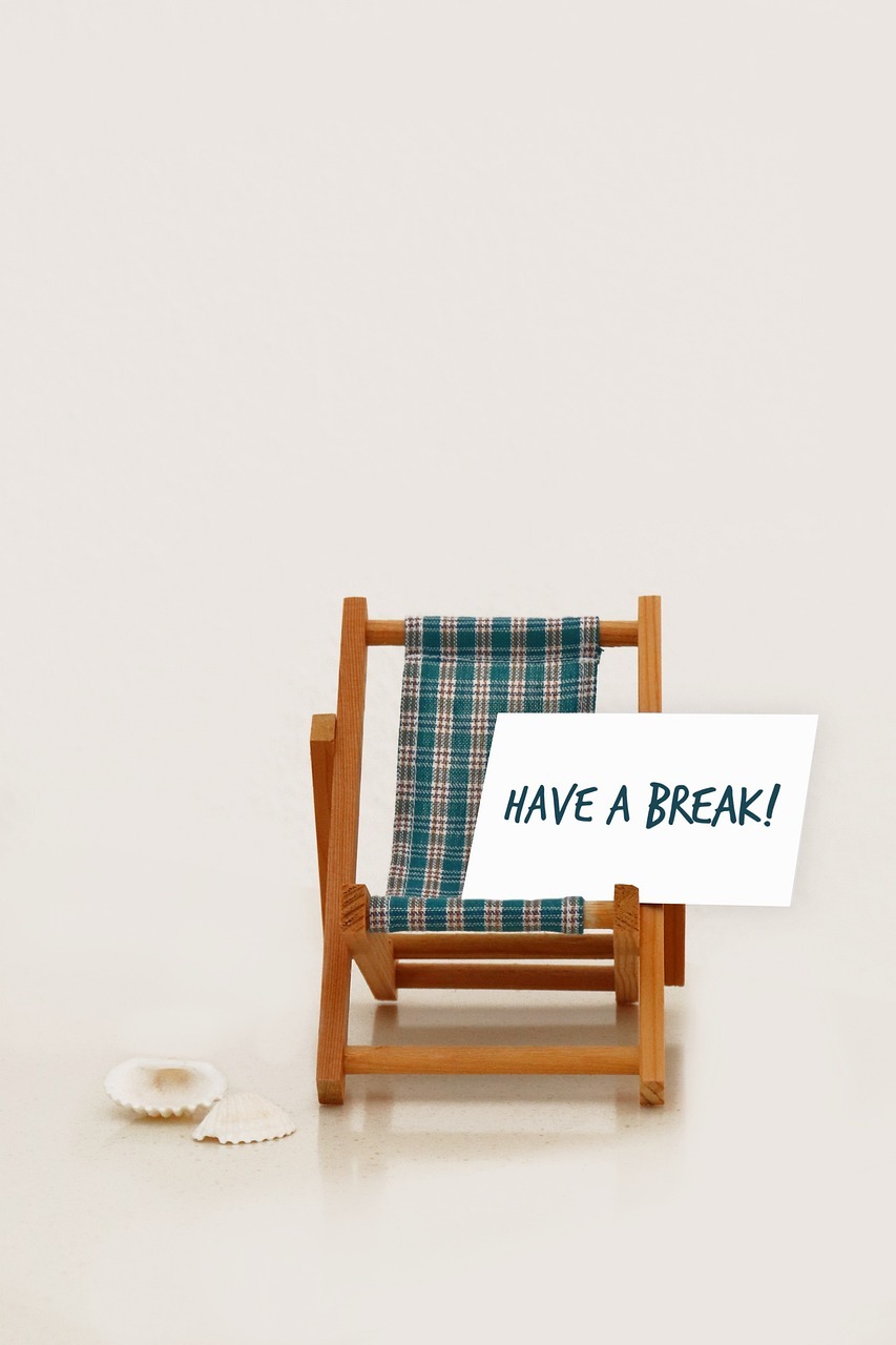 Symbolbild eines Miniaturliegestuhls mit einem Schild. Darauf steht: Have a Break! Nimm' eine Pause