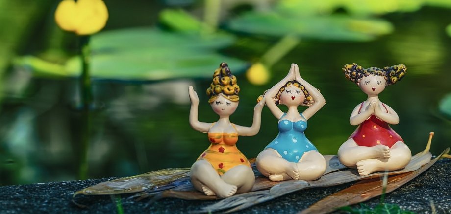 Drei kleine Frauenfiguren aus Ton sitzen auf einem Stock und meditieren.