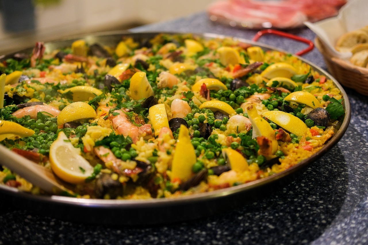 Nahaufnahme einer Paella-Pfanne mit Reis, Gemüse, Zitronen und weiteren Zutaten