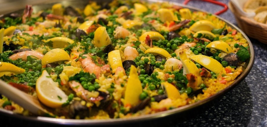 Nahaufnahme einer Paella-Pfanne mit Reis, Gemüse, Zitronen und weiteren Zutaten