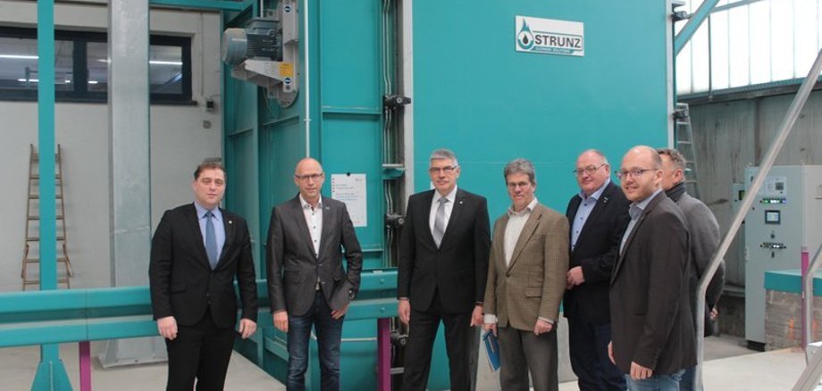 Fertig ist der Lack“ – hinter der saloppen Bezeichnung verbirgt sich ausgeklügelte Technik, um die jährliche CO2-Emission zu senken, erläutert Firmenchef Harald Schreiner (Zweiter von links), der Landrat Manfred Görig (Mitte) die neue Maschine zum Entfernen von Lackpartikeln vorstellt. Beim Rundgang werden Schreiner und Görig von Bürgermeister Lars Wicke, dem kaufmännischen Leiter von PBS, Thomas Schäfer, Manfred Schreiner (Firma GMS), Thomas Schaumberg (Vogelsberg Consult) und Sven Schreiner (GMS) begleitet.