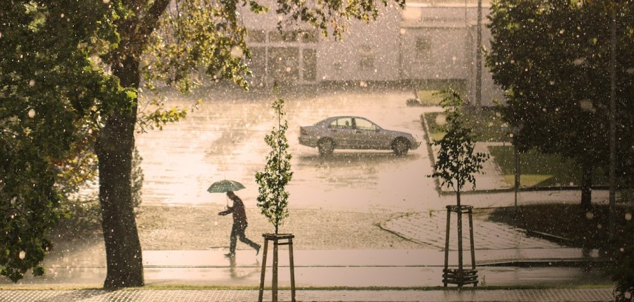 Ein Mann läuft mit Regenschirm auf einem Gehweg. Es regnet stark