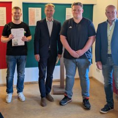 Landrat Dr. Jens Mischak, Vorstandsvorsitzender des Vereins Region Vogelsberg, und Edwin Schneider (rechts), Vorsitzender des LEADER-Beirats, überreichen Jonas Ruppel (links) und Lukas Schaub vom Jugend- und Kirmesclub Eichenrod den Zuwendungsvertrag.