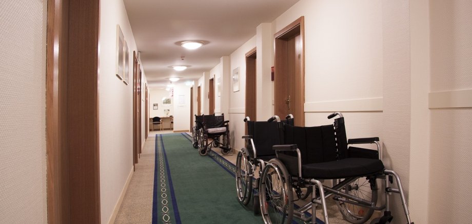 mehrere Rollstühle stehen an der Wand in einem langen Flur