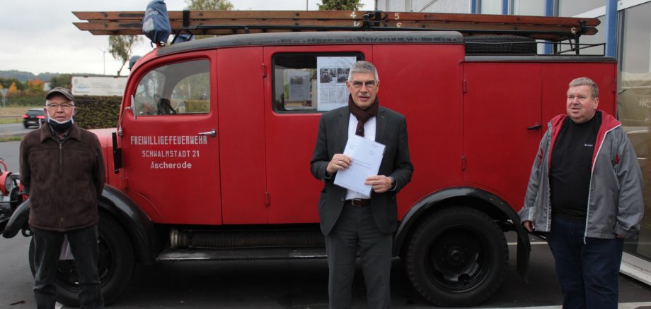 Landrat Görig und zwei Vereinsvertreter stehen vor einem 80 Jahre alten Feuerwehrauto