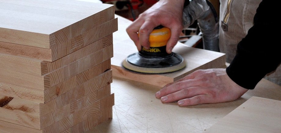 Ein Mensch schleift ein Holzteil mit einem Exzenterschleifer