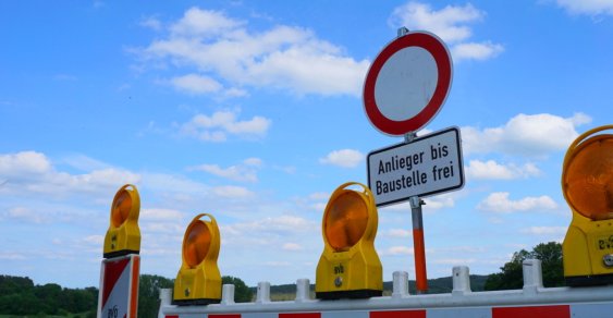 Eine Warnbarke mit Einfahrt Verboten Schild auf einer gesperrten STraße. Im Hintergrund ein blauer Himmel mit Wolken
