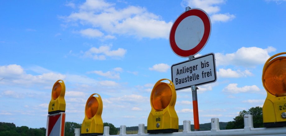 Eine Warnbarke mit Einfahrt Verboten Schild auf einer gesperrten STraße. Im Hintergrund ein blauer Himmel mit Wolken