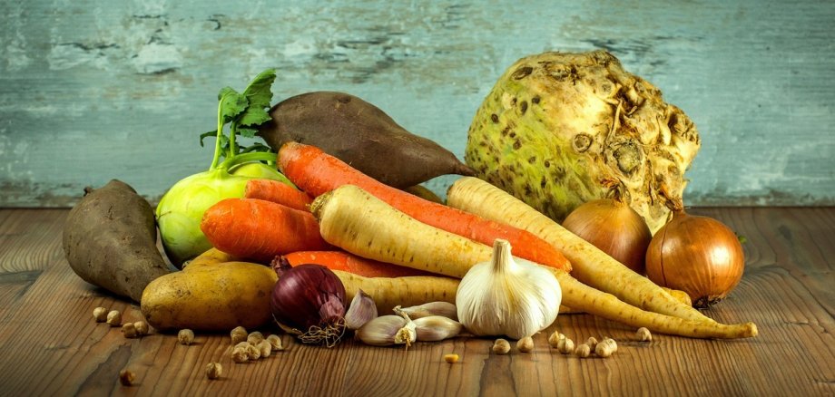 Verschiedene GEmüse, etwa Karotten, Zwiebeln, Rote Beete und Knoblauch liegen auf einem Holztisch.