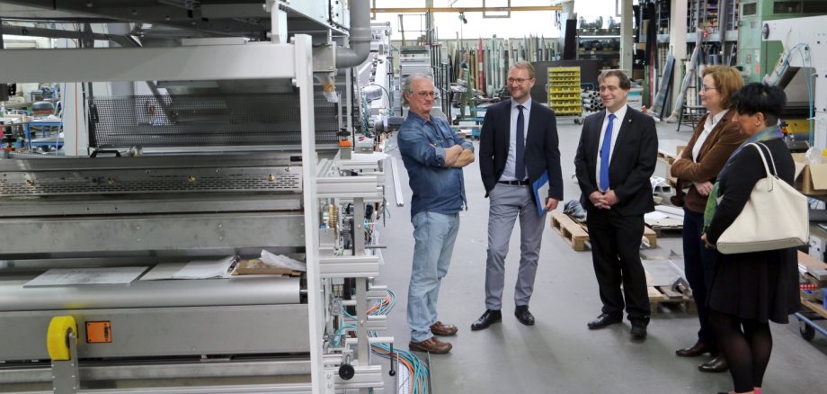 Die mehr als 30 Meter lange Rollen-/Inline-Kaschiermaschine soll noch vor Weihnachten in ihr neues Zuhause nach Polen umziehen, erklärt Geschäftsführer Günter Stock (v. l.) Wirtschaftsdezernent Jens Mischak, Bürgermeister Lars Wicke, Andrea Ortstadt (Wirtschaftsförderung) und Ute Müller (Arbeitgeberservice im Kommunalen Jobcenter KVA). 